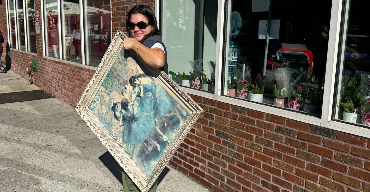 person carrying a large framed painting on the sidewalk