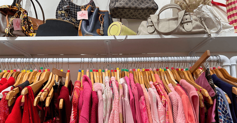 Red, pink, and purple vintage clothes on a rack with vintage purses displayed above