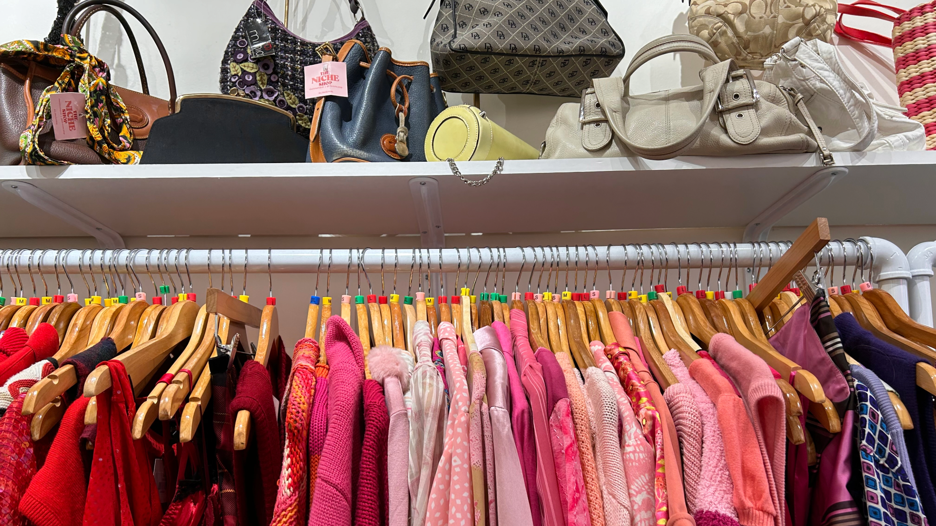 Red, pink, and purple vintage clothes on a rack with vintage purses displayed above